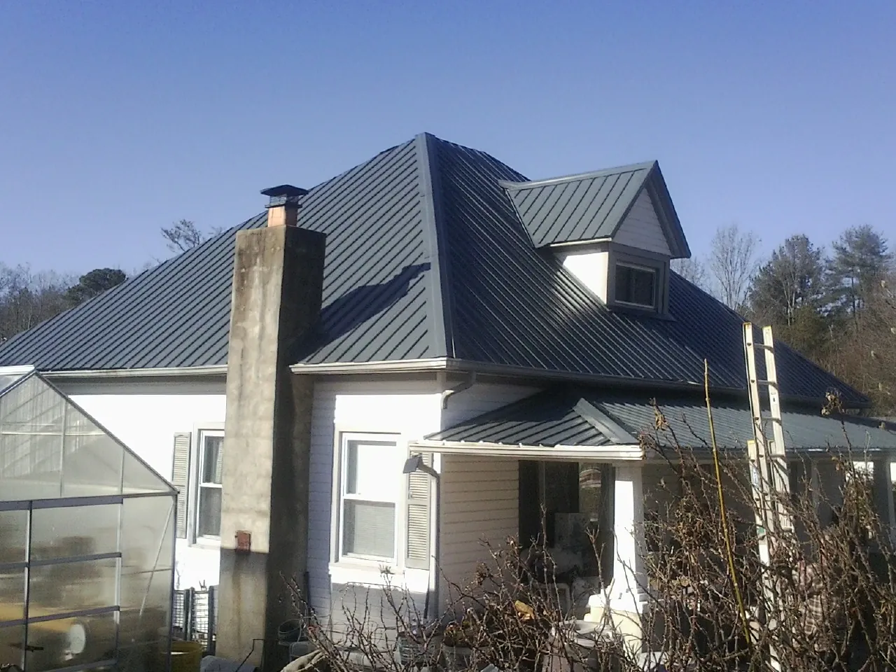 Dark blue standing seam metal roof on a white farmhouse with dormer — Slate & Tile Roof Repair by Roofing Brothers in Chadwicks