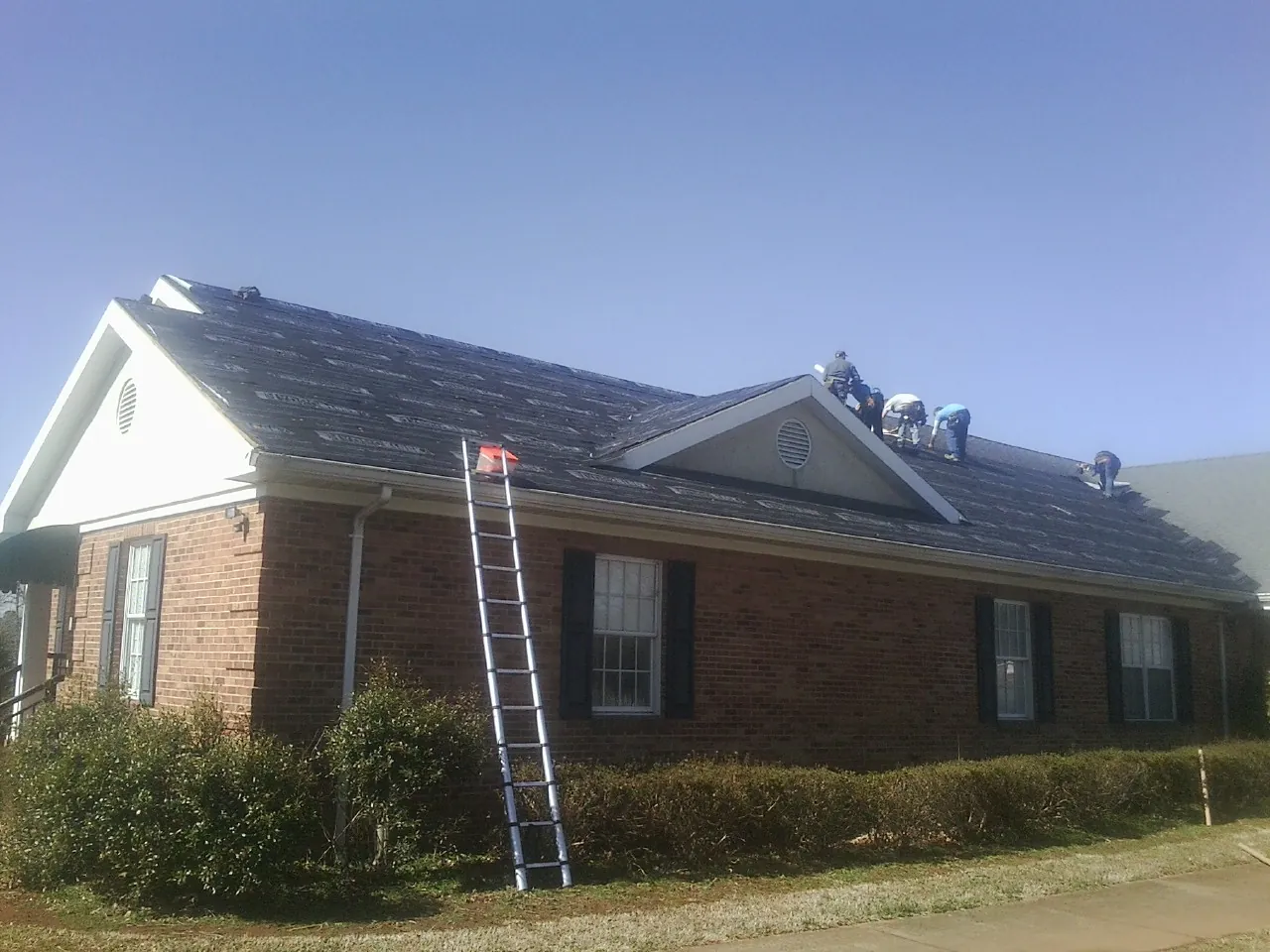 Crew tearing shingles off a brick ranch roof with a ladder set — Metal Roof Repair work by our crew in Chadwicks
