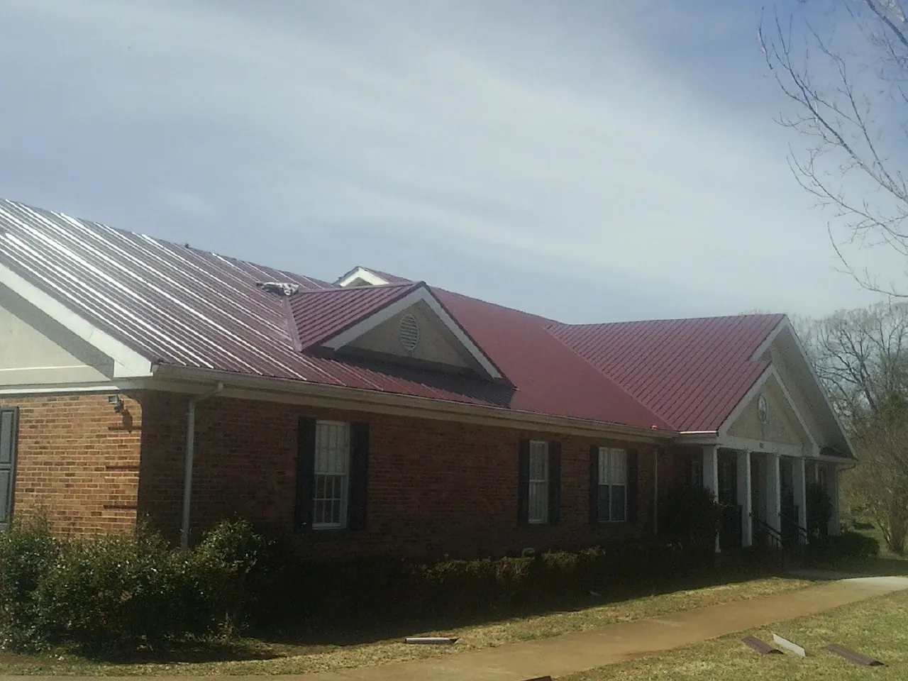 Red metal roof with gabled entries on a long brick building, from a Hail Damage Roof Repair job in Chadwicks