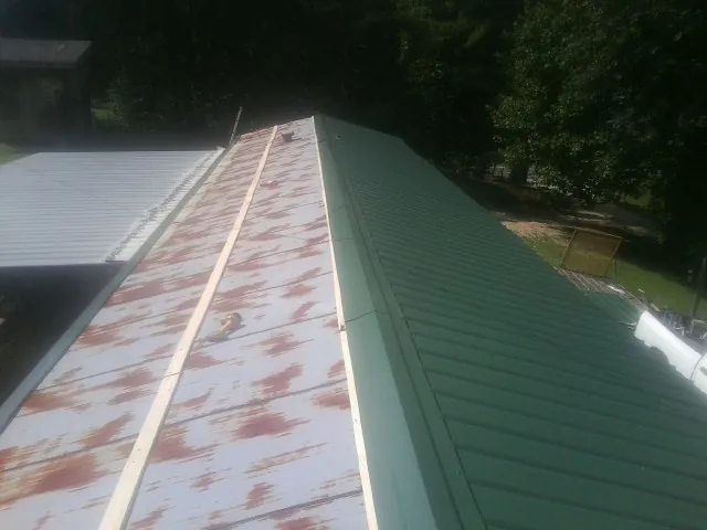 Old rusted panels beside newly installed green metal roofing — Wind Damage Roof Repair by Roofing Brothers in Chadwicks