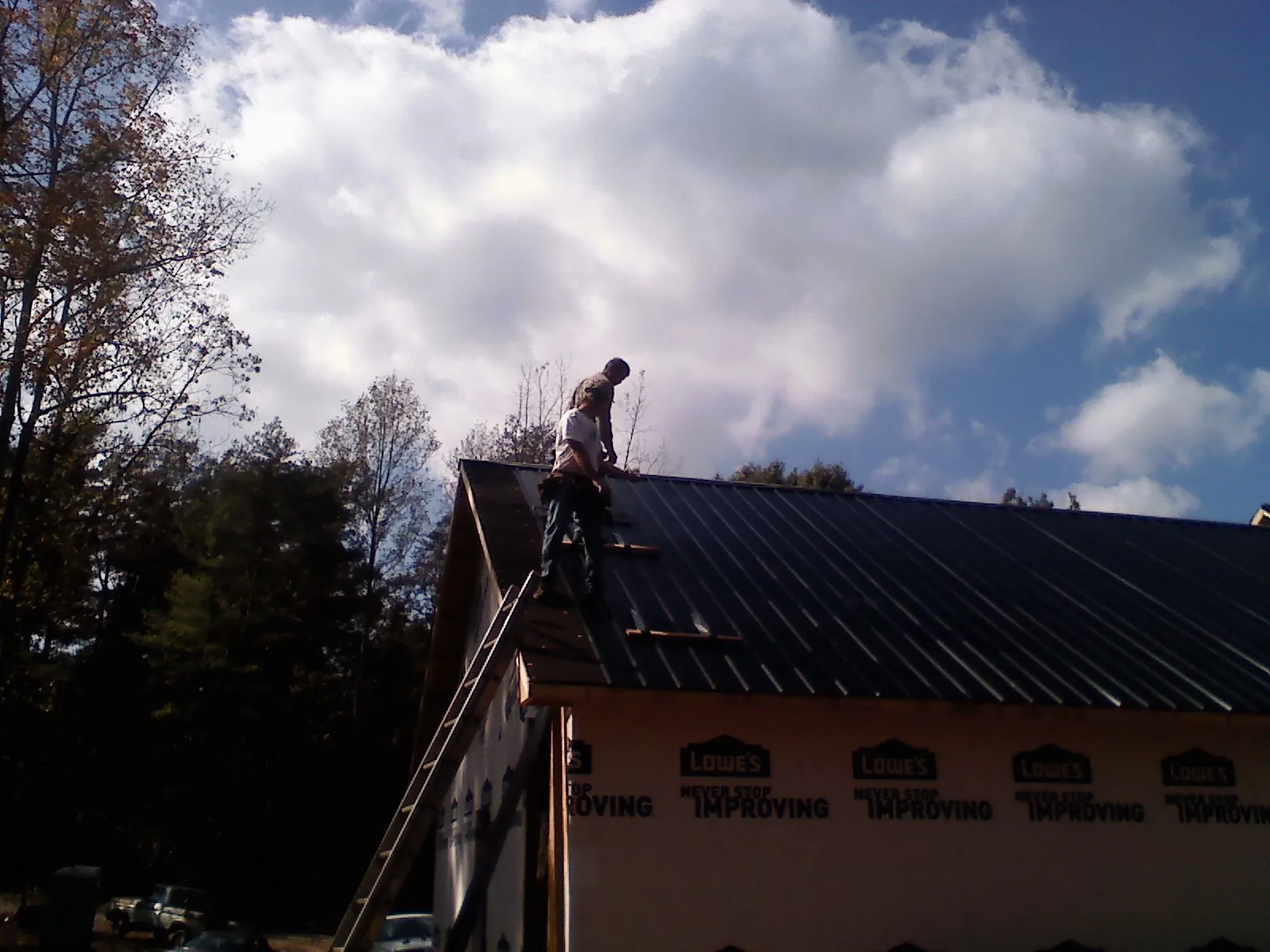 Roofer fastening dark metal panels high against a cloudy sky, from a Roof Inspection job in Chadwicks
