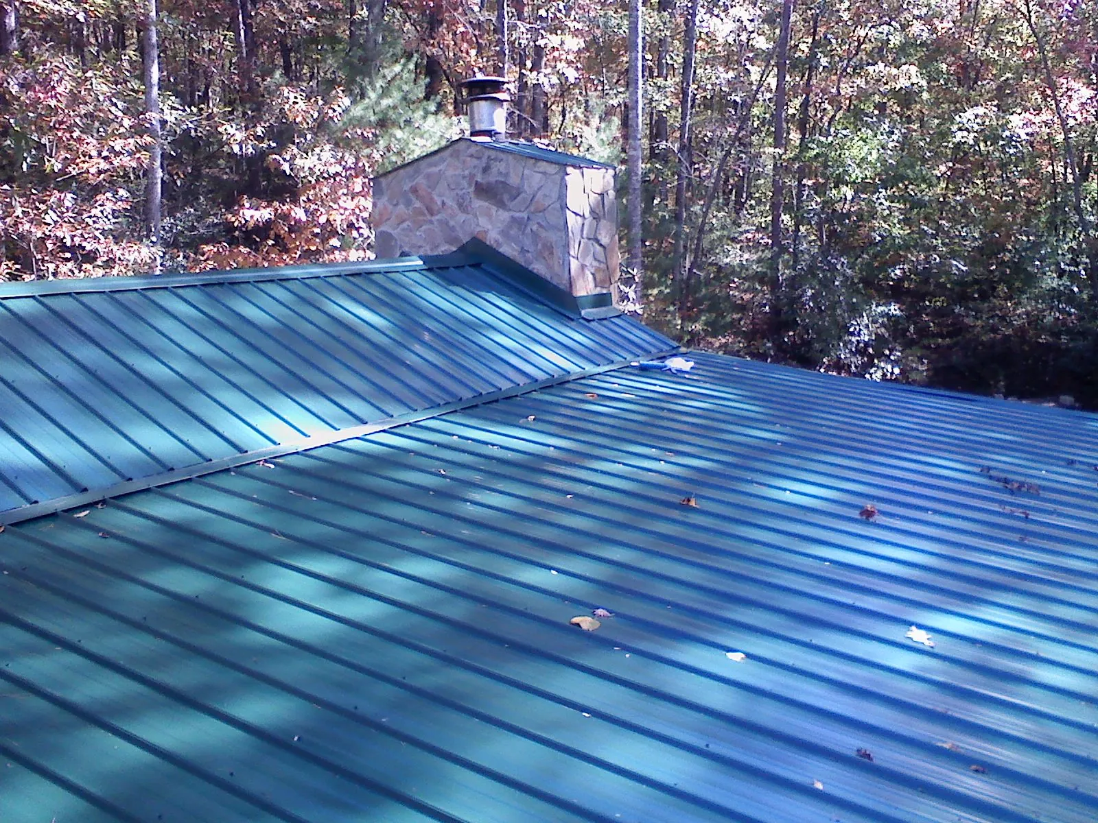 New green metal roof and stone chimney surrounded by autumn woods in Chadwicks