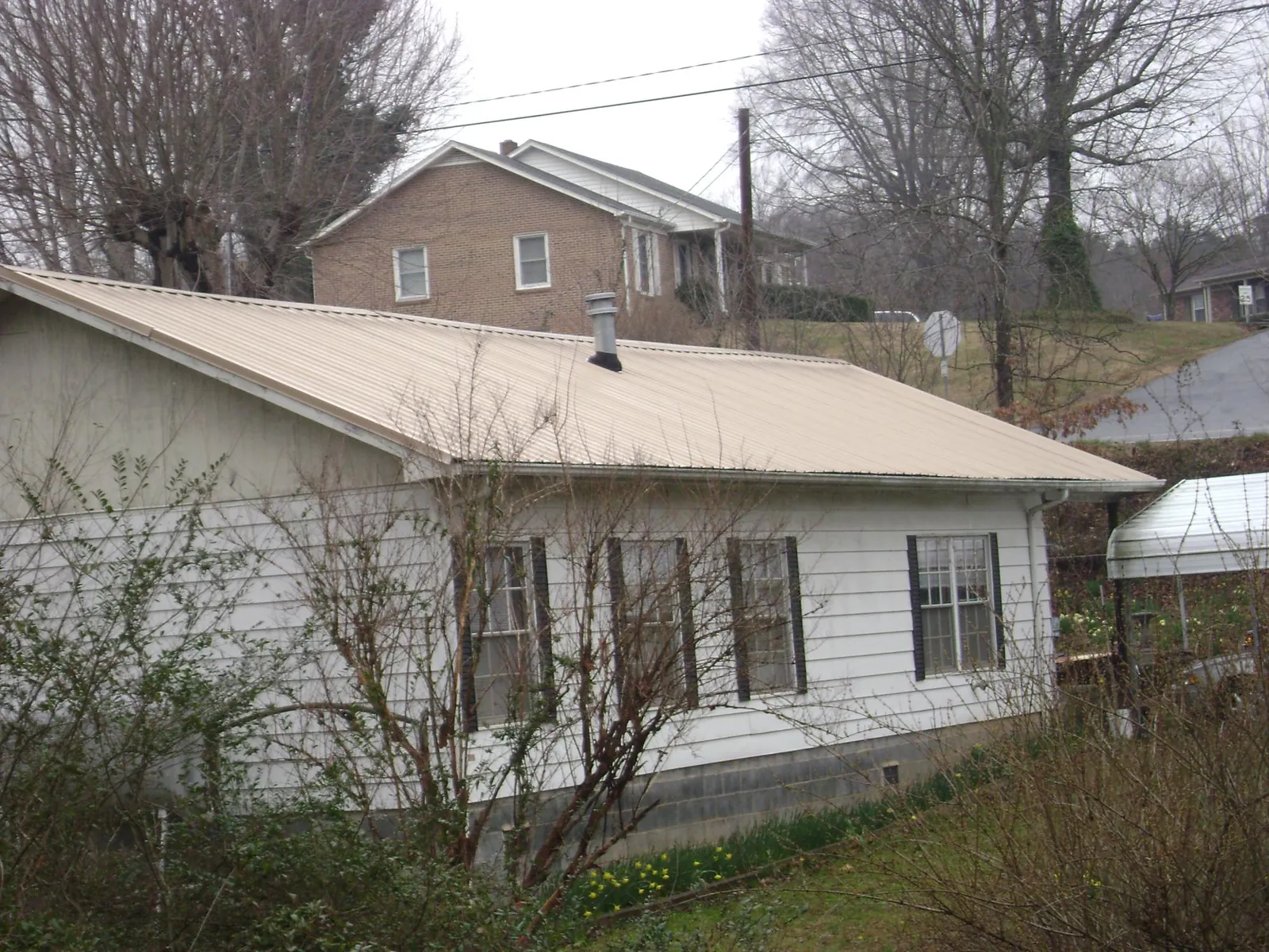 Tan metal roof on a white sided house set into a hillside — Commercial Roofing by Roofing Brothers in Chadwicks