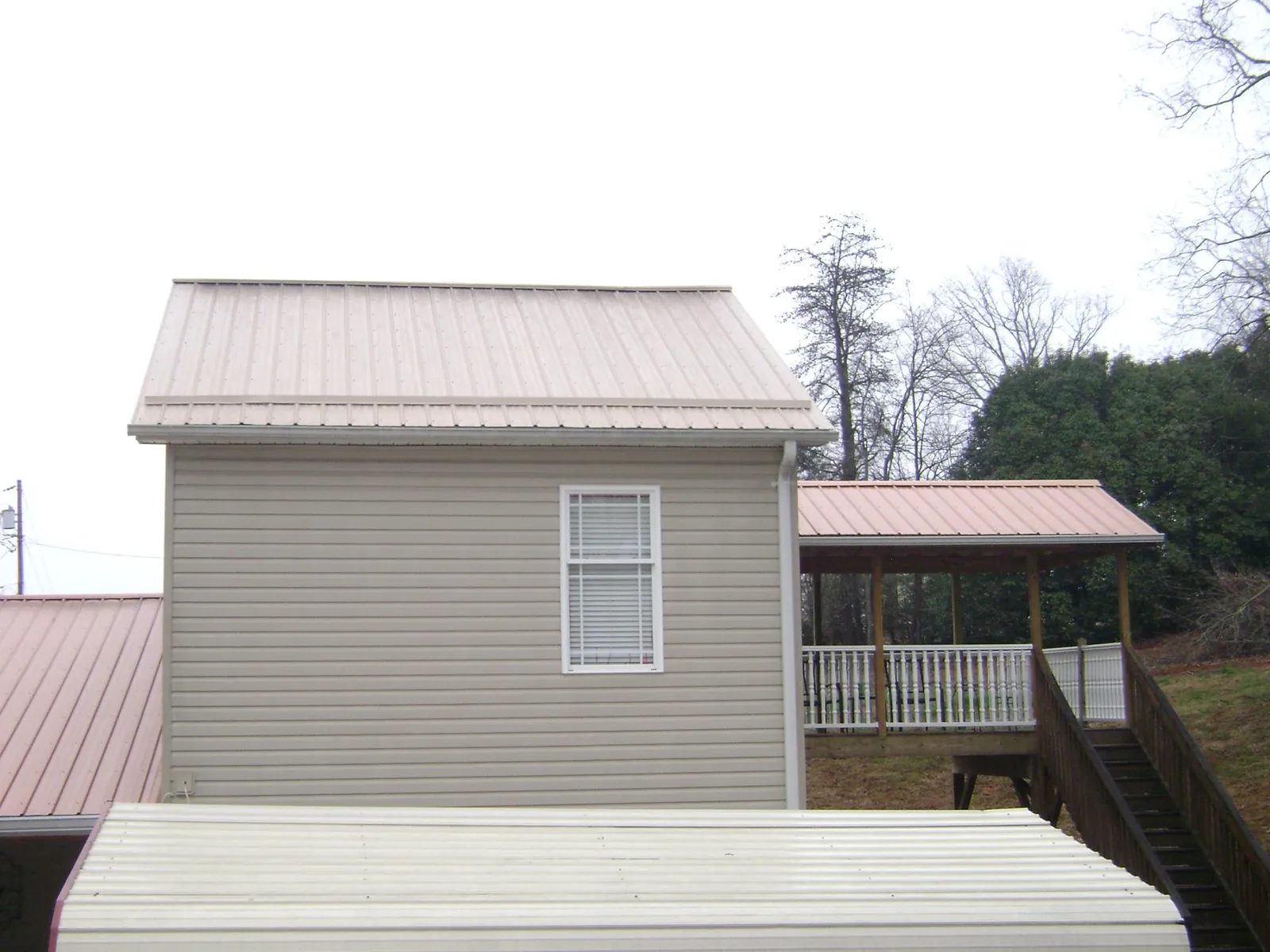 Tan metal roofs on a two story addition and attached porch, from a Roof Replacement job in Chadwicks